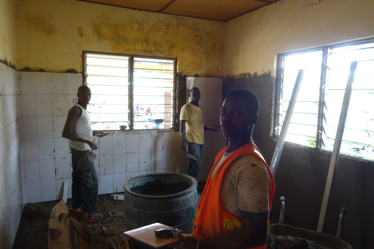 Three tile workers setting floor tiles in a clinic during a construction project
