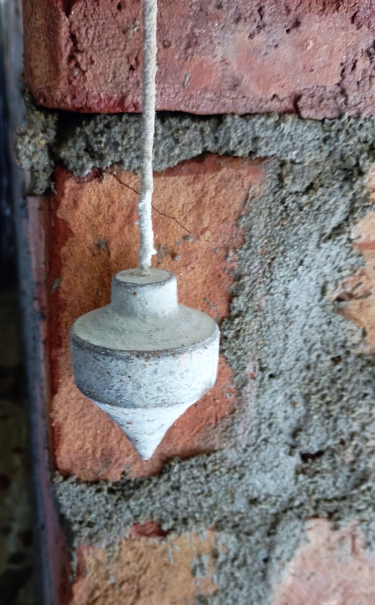 A traditional brass plumb bob hanging from a string to check vertical alignment